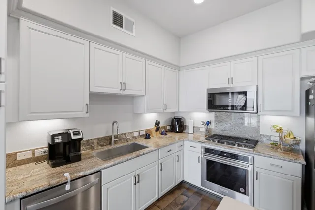 a kitchen with granite countertop white cabinets sink and stainless steel appliances