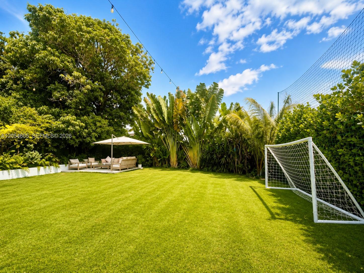 3538 Southwest 1st Avenue, Unit 1 Miami, FL 33145 - Photo 8 of 20 Spacious patio and backyard area featuring a large open lawn, lush tropical landscaping, and a cozy covered seating area ideal for relaxing or entertaining. The expansive green space offers plenty of room for outdoor activities, while the soccer goal and surrounding privacy hedges create a fun, private, and family-friendly outdoor setting.