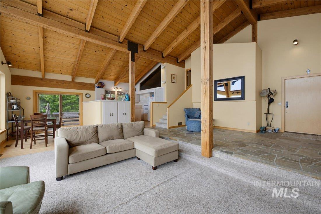 3800 Warren Wagon Road McCall, ID 83638 - Photo 50 of 50 Vaulted wood plank ceiling with exposed beams, sliding glass door, a dining area with a wood table and chairs, a kitchen area with white cabinetry, and a split-level floor plan with flagstone flooring