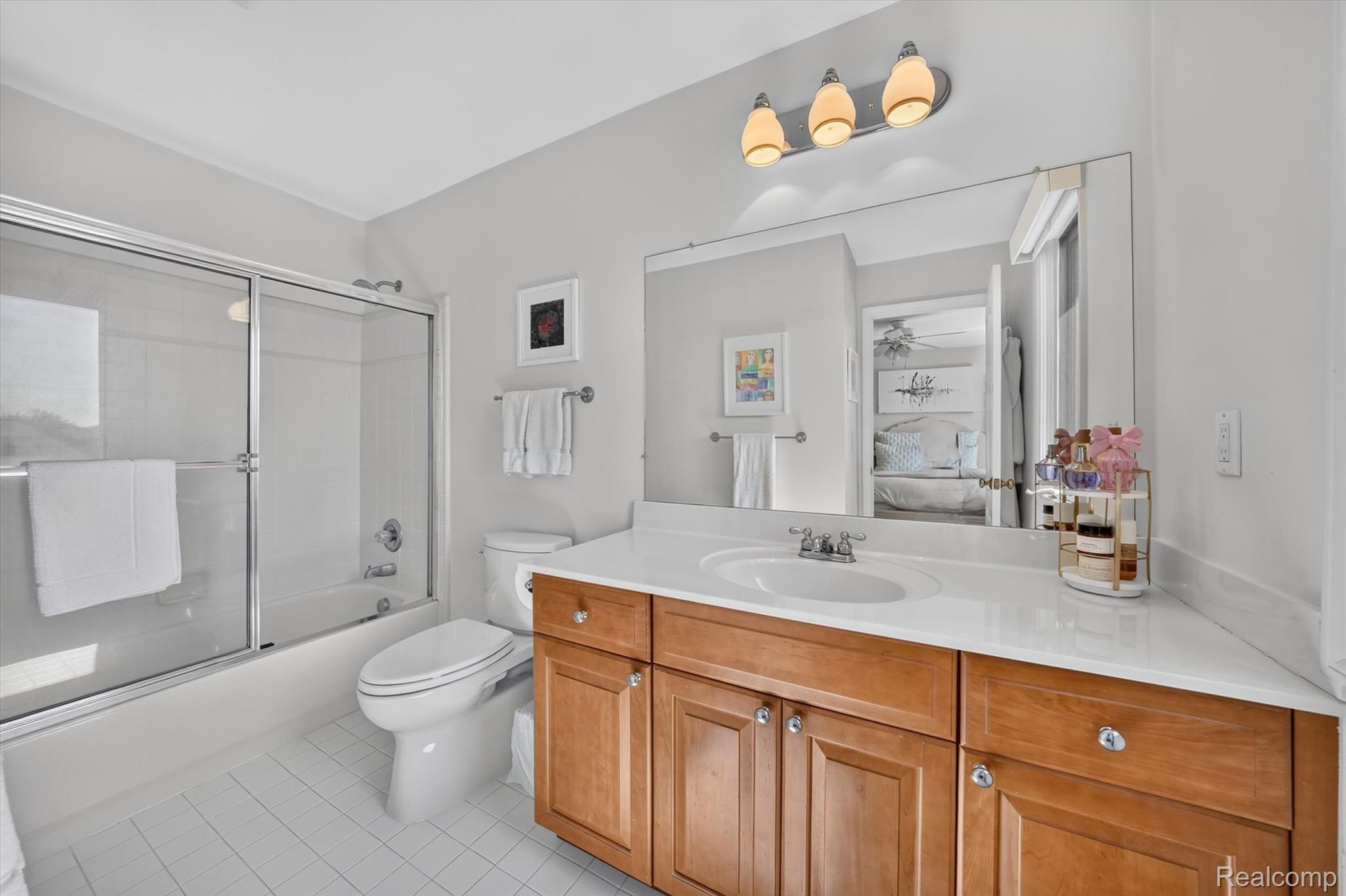 3804 Elk Drive Rochester, MI 48306 - Photo 34 of 75 Bathroom featuring a wood-finish vanity with a white countertop, an integrated sink, a large wall-mounted mirror, and a tub with a sliding glass door enclosure
