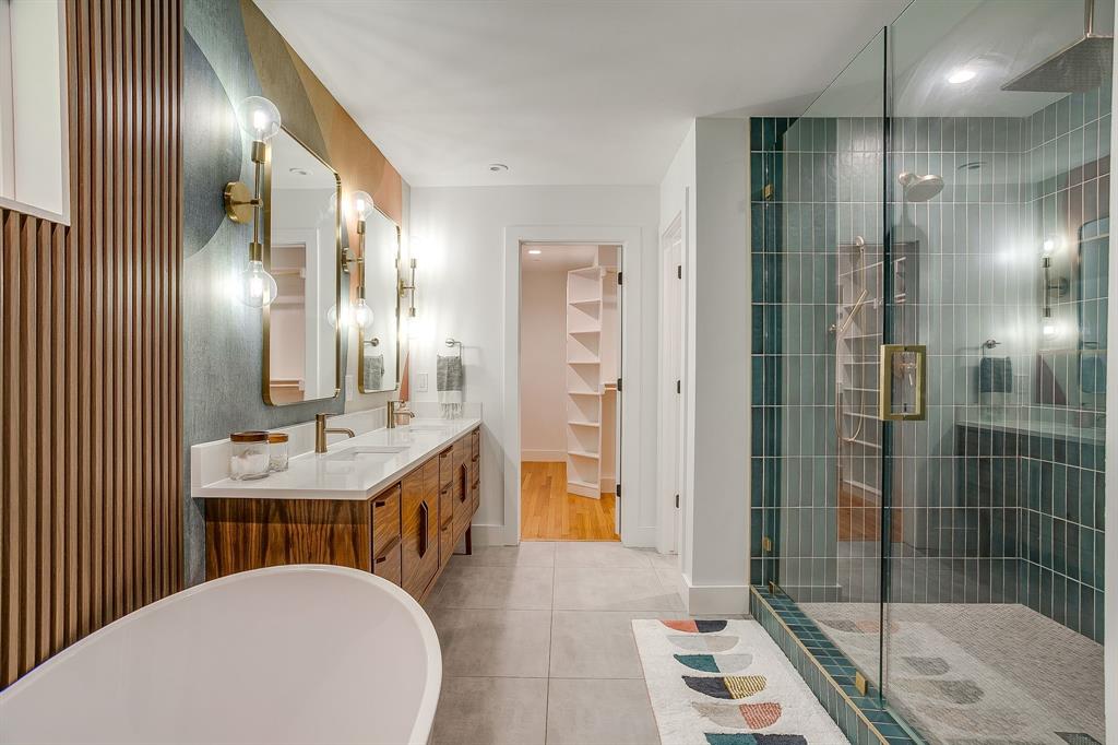 6700 Fortune Road Fort Worth, TX 76116 - Photo 26 of 40 Spacious bathroom featuring a freestanding soaking tub, a dual vanity with quartz countertop, a walk-in shower with glass enclosure and vertical tile, and built-in shelving