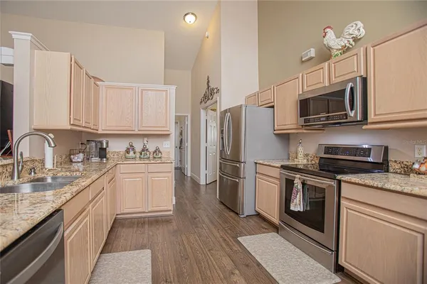 a kitchen with stainless steel appliances granite countertop a sink a stove top oven a refrigerator with white cabinets and wooden floor