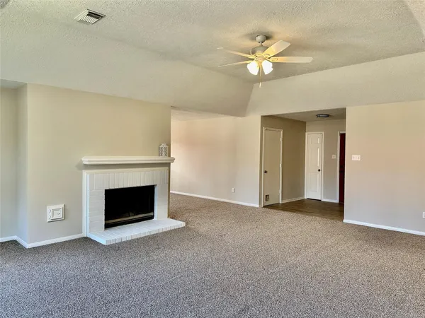 a view of an empty room with chandelier fan and fire place