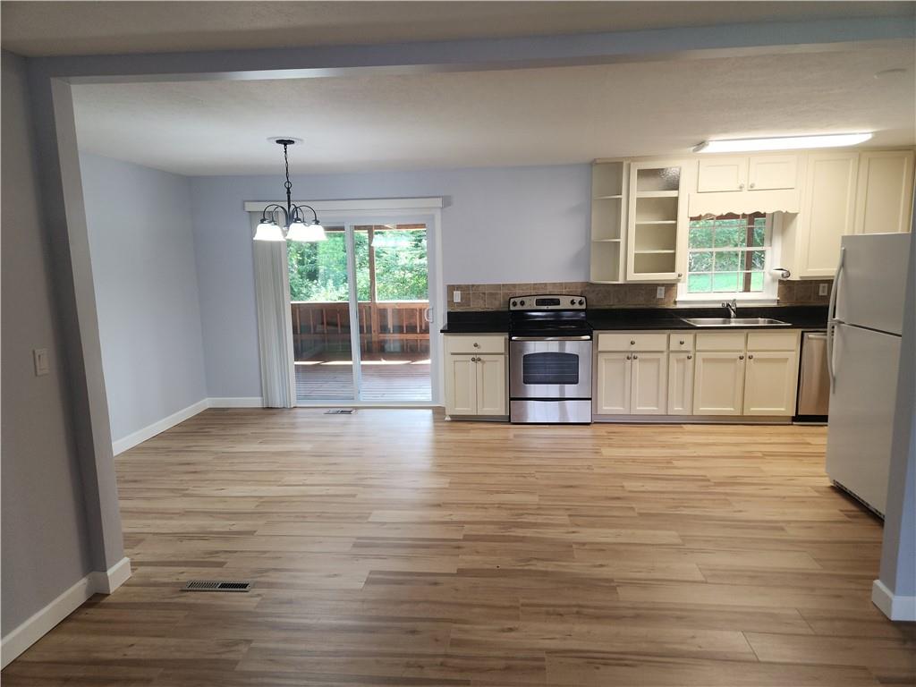 a kitchen with stainless steel appliances granite countertop a stove a sink dishwasher a refrigerator white cabinets and wooden floor