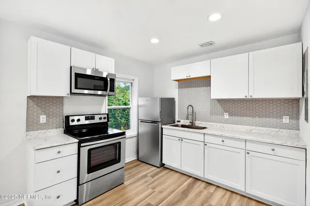 a kitchen with white cabinets stainless steel appliances and wooden floor