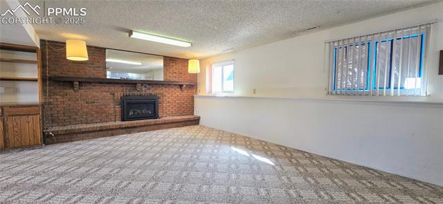 6313 Chippewa Road Colorado Springs, CO 80915 - Photo 30 of 36 Unfurnished living room featuring light carpet, a fireplace, and a textured ceiling