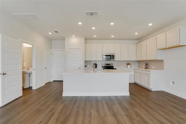 a large white kitchen with wooden floors stainless steel appliances and cabinets