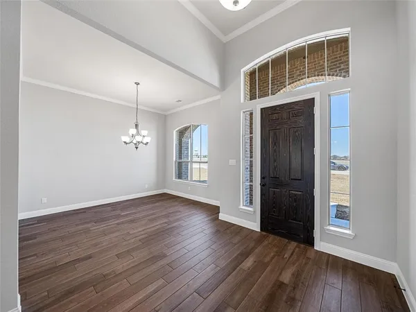 an empty room with wooden floor chandelier and windows