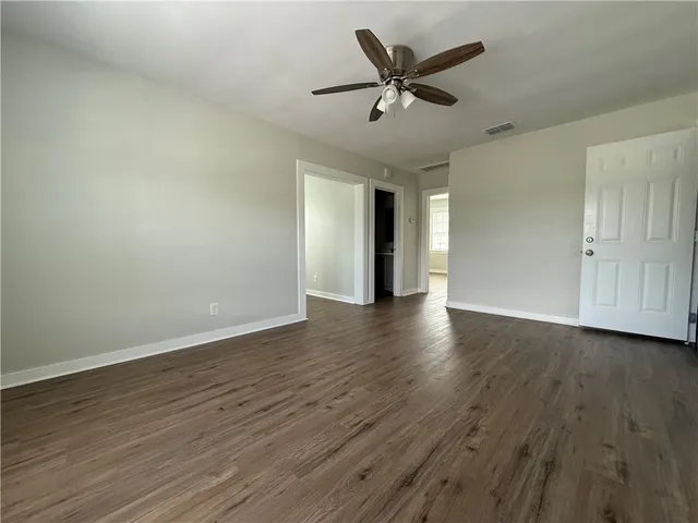 a view of an empty room with wooden floor and a ceiling fan