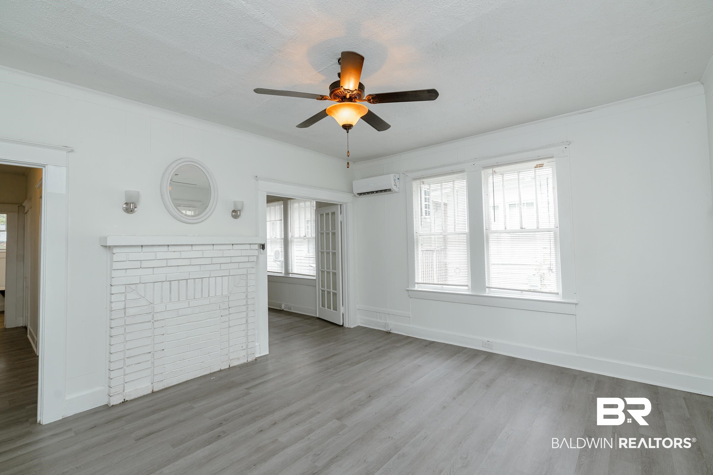 5 North Fulton Street Mobile, AL 36607 - Photo 38 of 55 Unfurnished living room with a wall mounted AC, ceiling fan, a fireplace, crown molding, and light hardwood / wood-style flooring