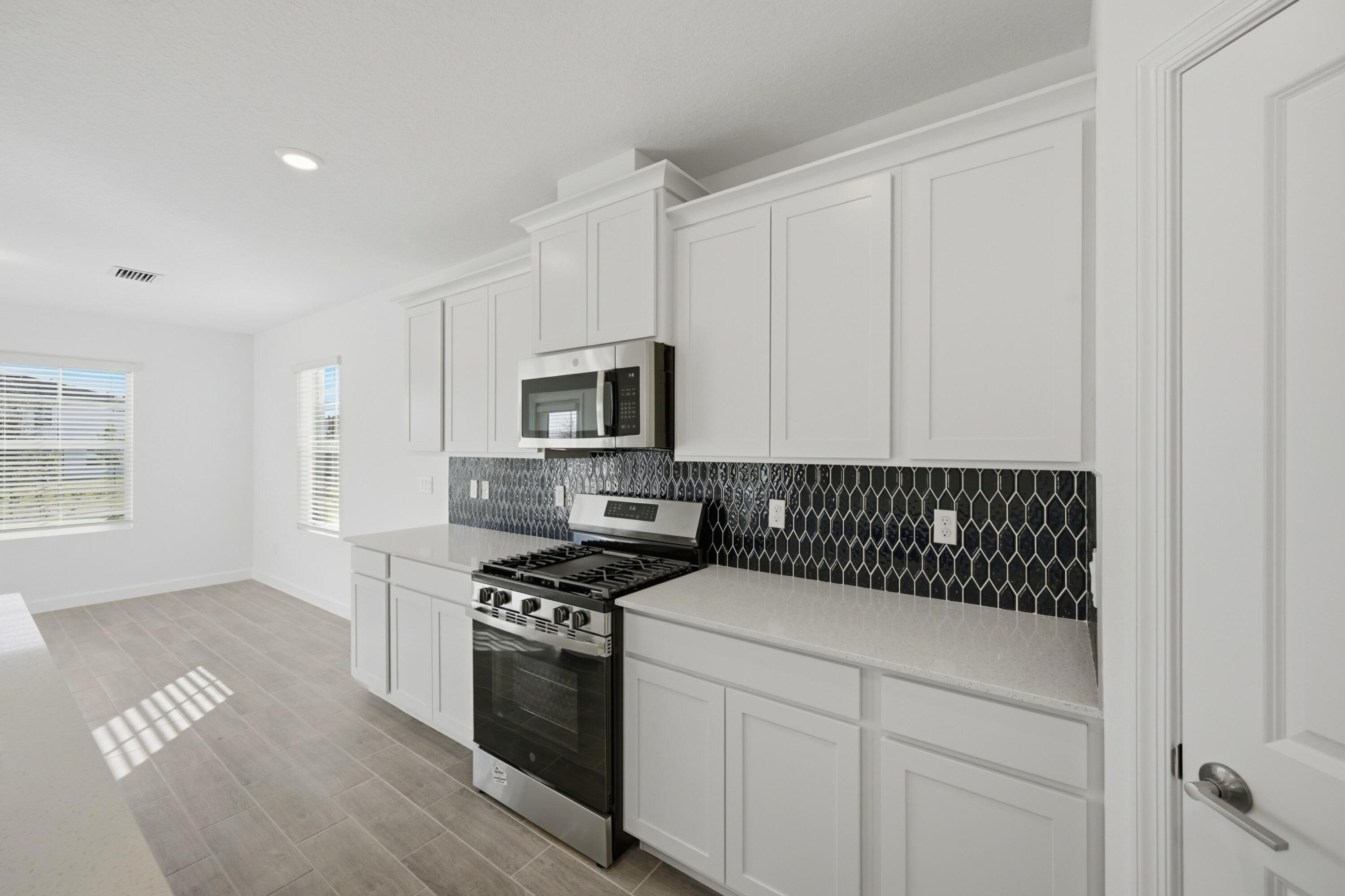 19568 Whispering Creek Road Loxahatchee, FL 33470 - Photo 9 of 30 a kitchen with stainless steel appliances a stove a microwave and white cabinets