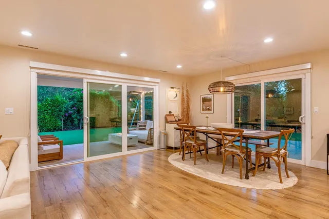 a view of a patio with lawn chairs floor to ceiling window plants and trees