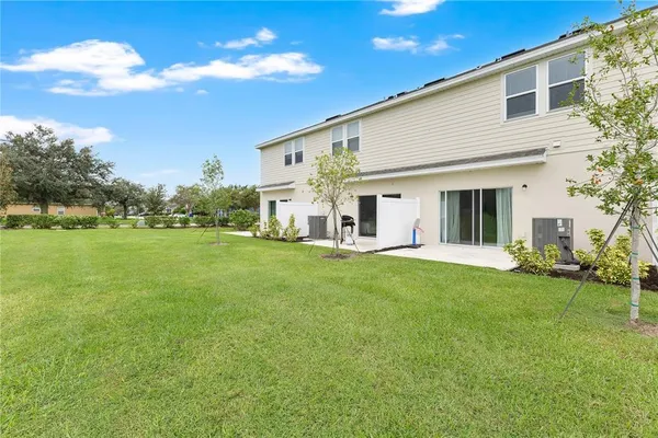 a view of a white house in front of a big yard with plants and large trees