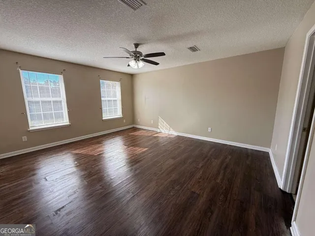 a view of an empty room with wooden floor and a ceiling fan