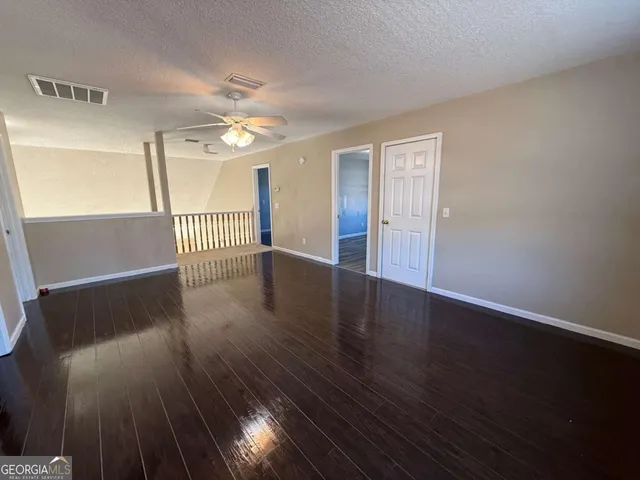 a view of an empty room with wooden floor and a ceiling fan