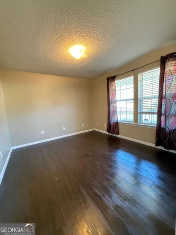 an empty room with wooden floor and windows with curtains