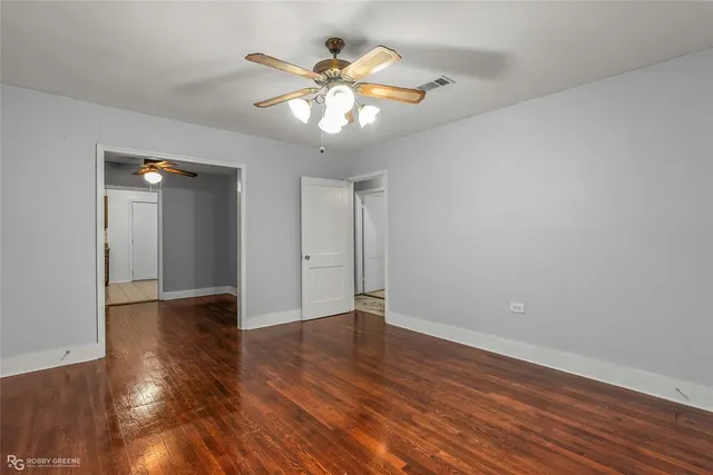 a view of an empty room with wooden floor and a ceiling fan