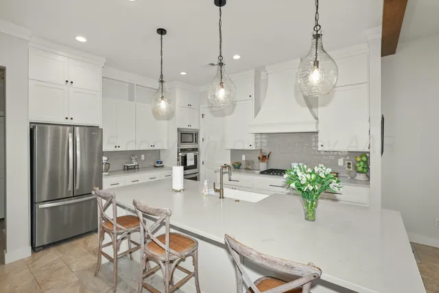 a kitchen with stainless steel appliances granite countertop a refrigerator a sink a stove a chandelier a dining table and chairs