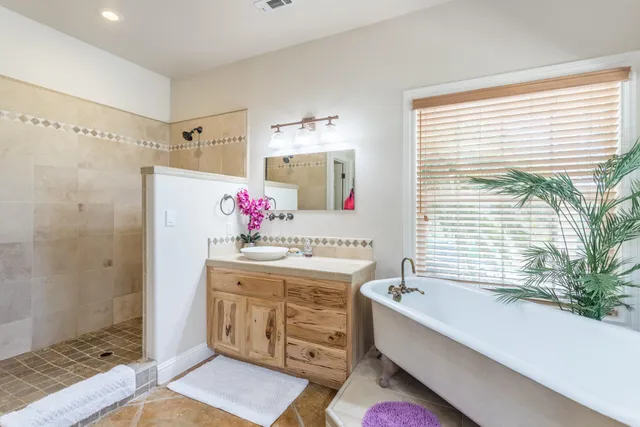 a spacious bathroom with a double vanity sink a large mirror a bathtub and next to a window