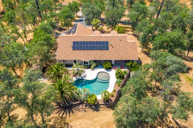 an aerial view of a house with swimming pool and large trees