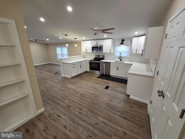 a large white kitchen with a white countertops a stove a couch and a dining table with wooden floor
