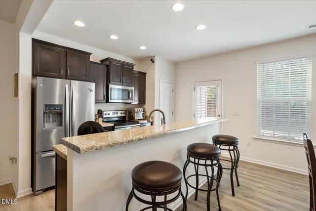 a kitchen with stainless steel appliances granite countertop a refrigerator a stove a sink cabinets and a dining table with wooden floor