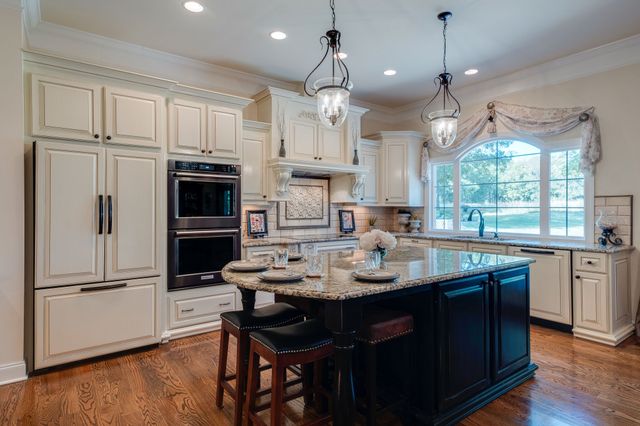 a kitchen with stainless steel appliances kitchen island granite countertop a refrigerator a sink dishwasher a stove and white cabinets with wooden floor