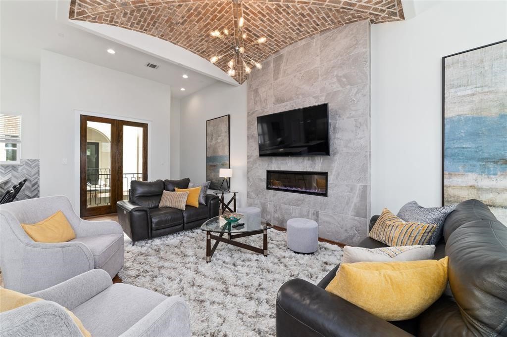 710 Delano Street, Unit A Houston, TX 77003 - Photo 6 of 32 This inviting living room features a vaulted brick ceiling, a modern stone accent wall with a built-in fireplace and TV, cozy seating with stylish cushions, and natural light from double doors. A plush carpet completes the warm, elegant aesthetic.