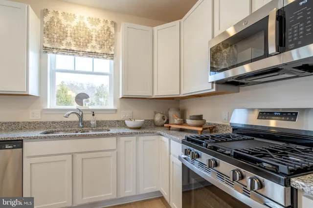 a kitchen with stainless steel appliances granite countertop white cabinets and a stove top oven