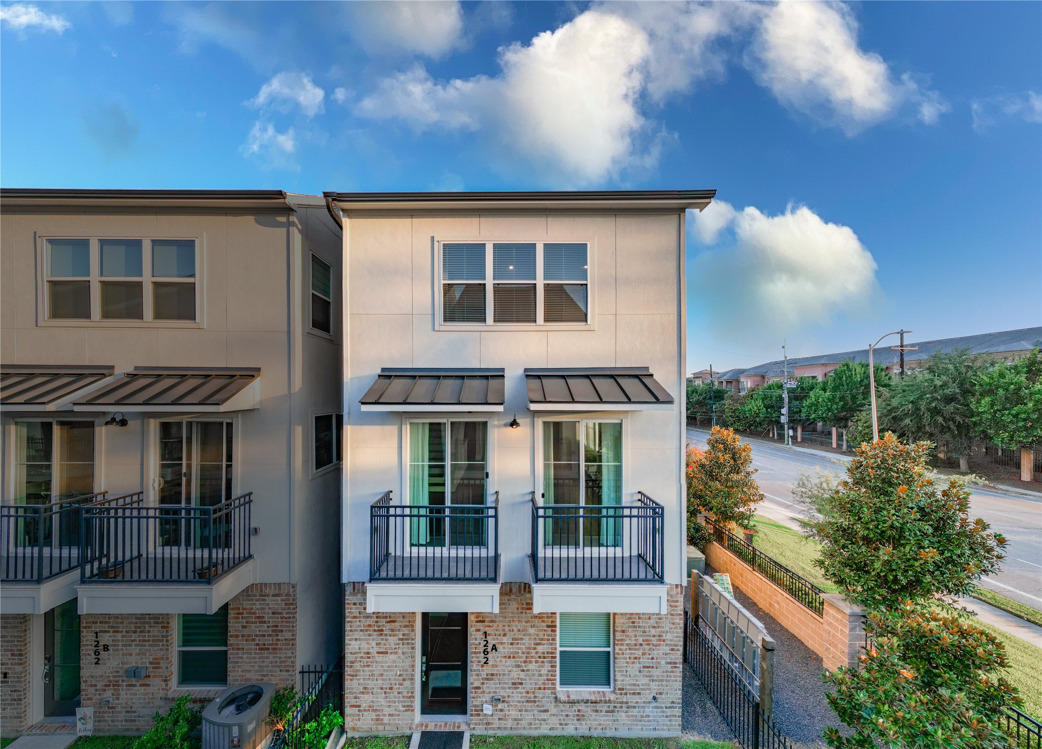 1262 North Post Oak Road, Unit A Houston, TX 77055 - Photo 1 of 50 This elevated front shot highlights the modern three-story townhouse featuring a classic brick base, white stucco upper floors, and dual private balconies. A neatly landscaped side yard with a decorative stone pathway adds vibrant curb appeal along the adjacent street.