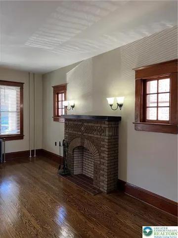 an empty room with wooden floor fireplace and windows