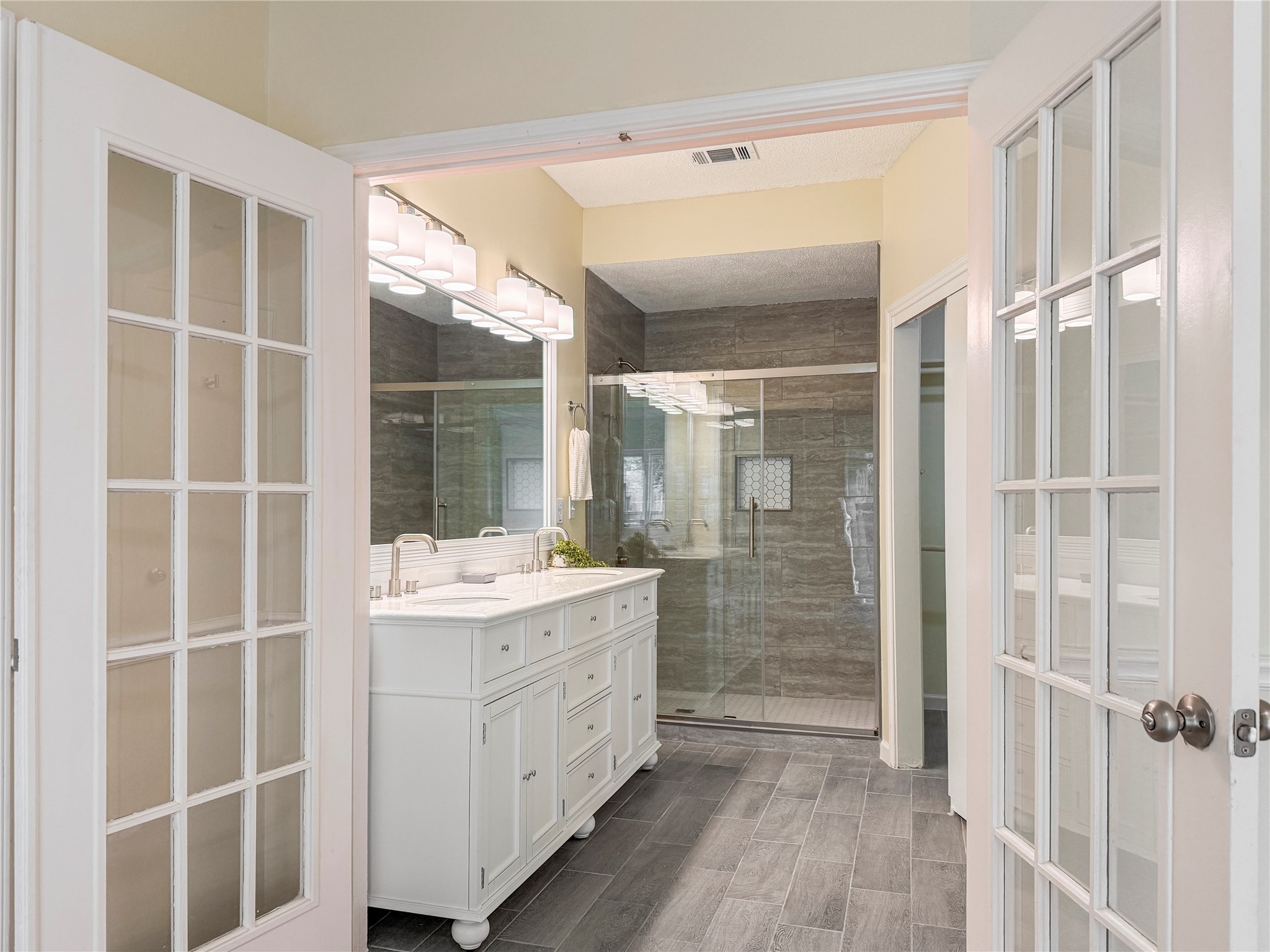 13635 Repa Lane Houston, TX 77014 - Photo 29 of 49 This bathroom features a modern design with a spacious glass-enclosed shower, stylish tile flooring, and a double-sink vanity with ample storage. French doors add elegance and natural light.