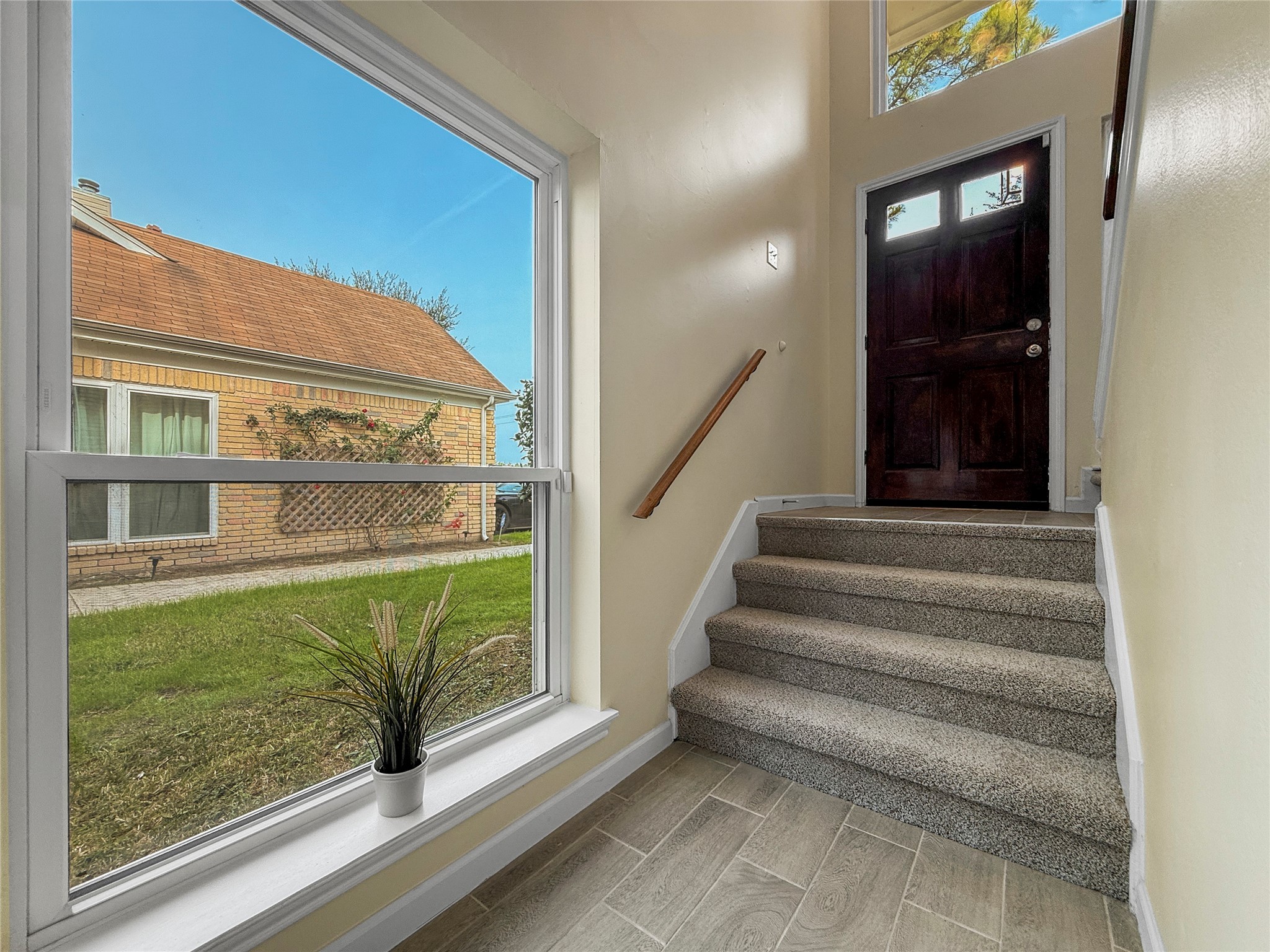 13635 Repa Lane Houston, TX 77014 - Photo 34 of 50 Are you ready to explore what is upstairs? Let's walk back towards the welcoming entryway with carpeted stairs. A large window offers natural light and views of the grassy exterior, creating a bright and inviting atmosphere.