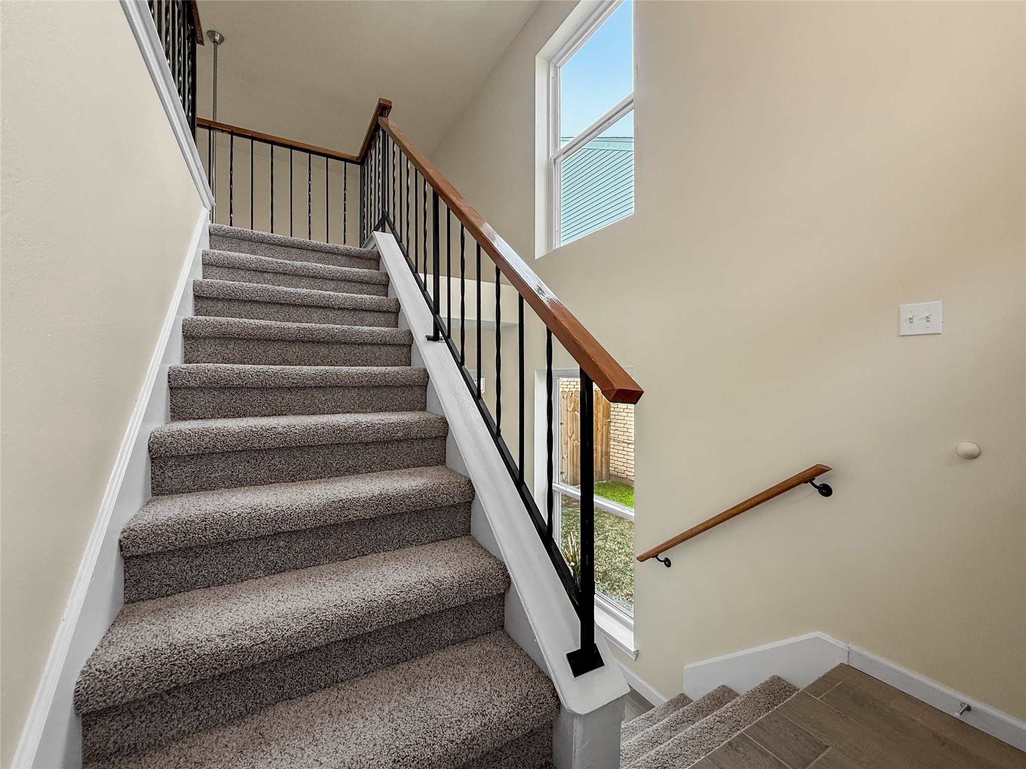 13635 Repa Lane Houston, TX 77014 - Photo 35 of 50 Going up, we find a carpeted staircase with a wooden handrail and black metal balusters. It features a large window on the landing, allowing natural light to brighten the area and offering a view of the outside.