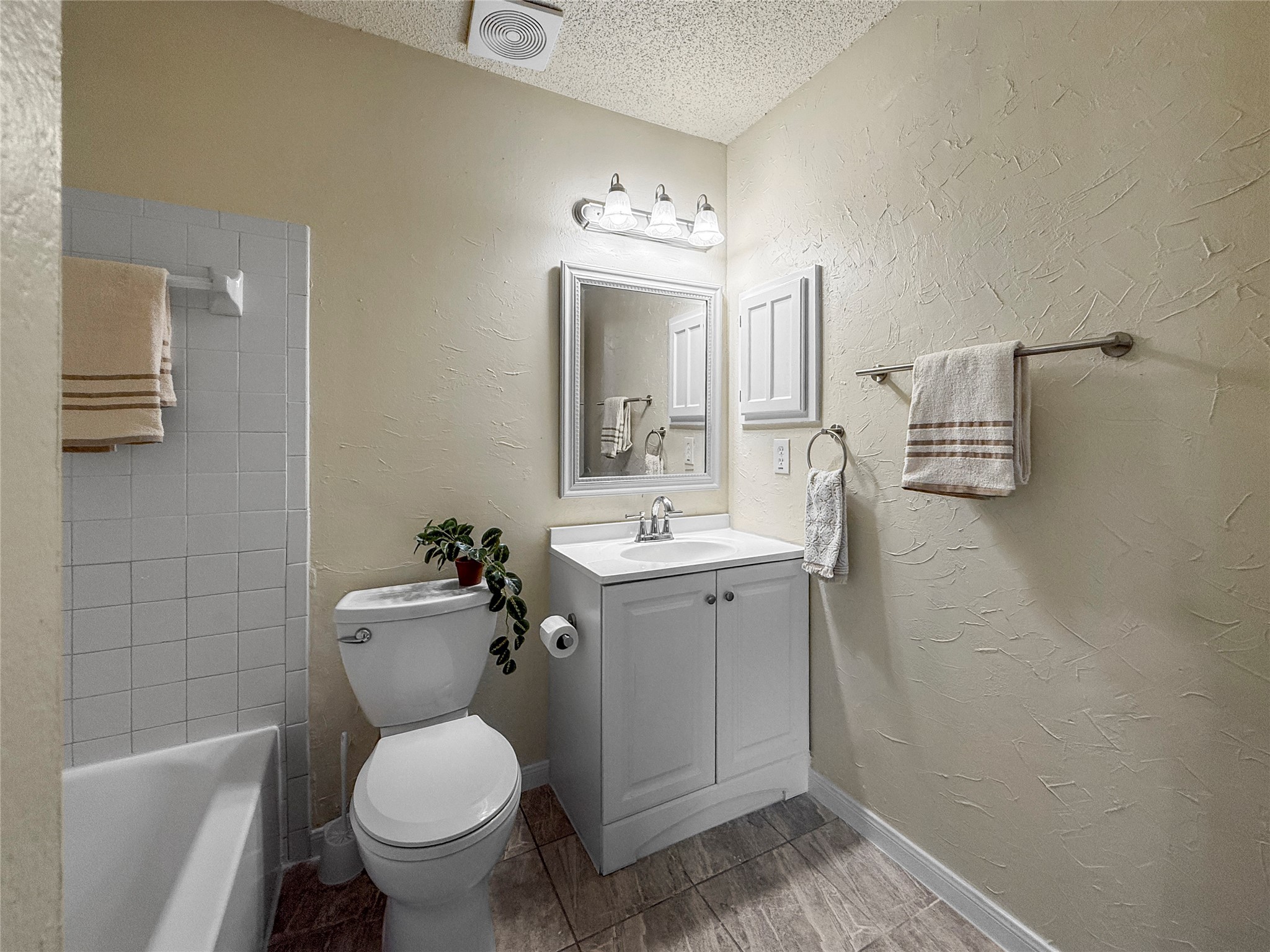 13635 Repa Lane Houston, TX 77014 - Photo 43 of 50 This bathroom features a clean, modern design with a white vanity and mirror, a standard toilet, and a bathtub with tiled walls. Neutral tones and textured walls add warmth, while ample lighting and a towel rack enhance functionality.