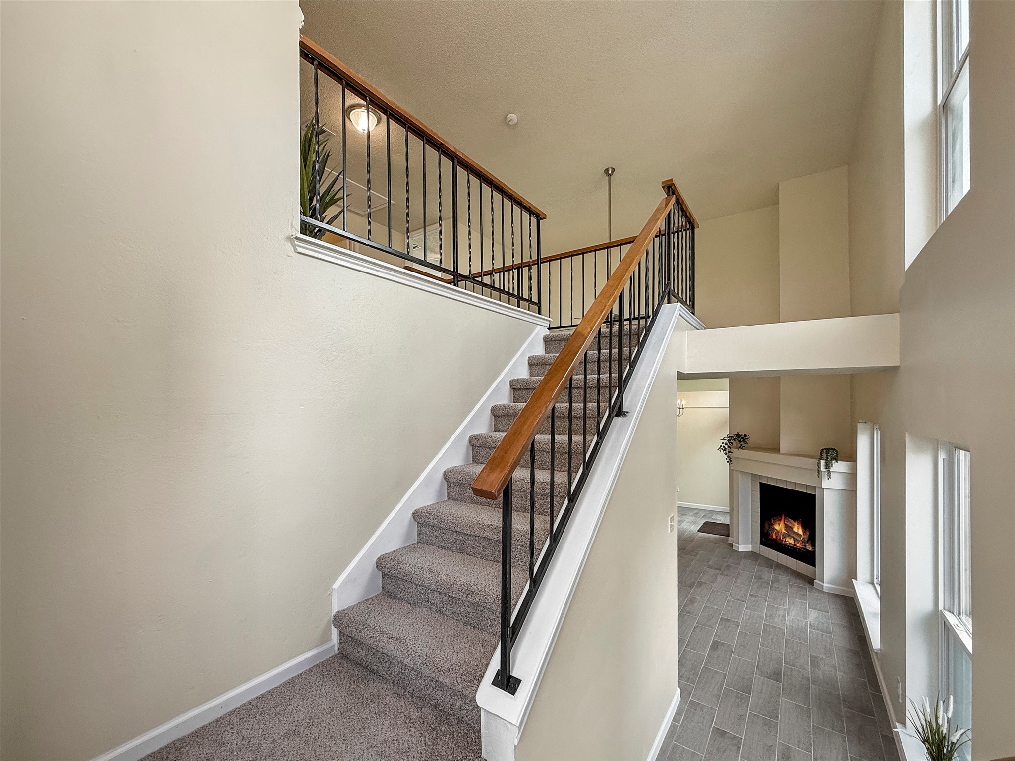 13635 Repa Lane Houston, TX 77014 - Photo 6 of 49 This photo showcases a bright, open staircase with a modern railing leading to an upper level. The lower area features a cozy living space with a fireplace and large windows, offering a welcoming and airy atmosphere.
