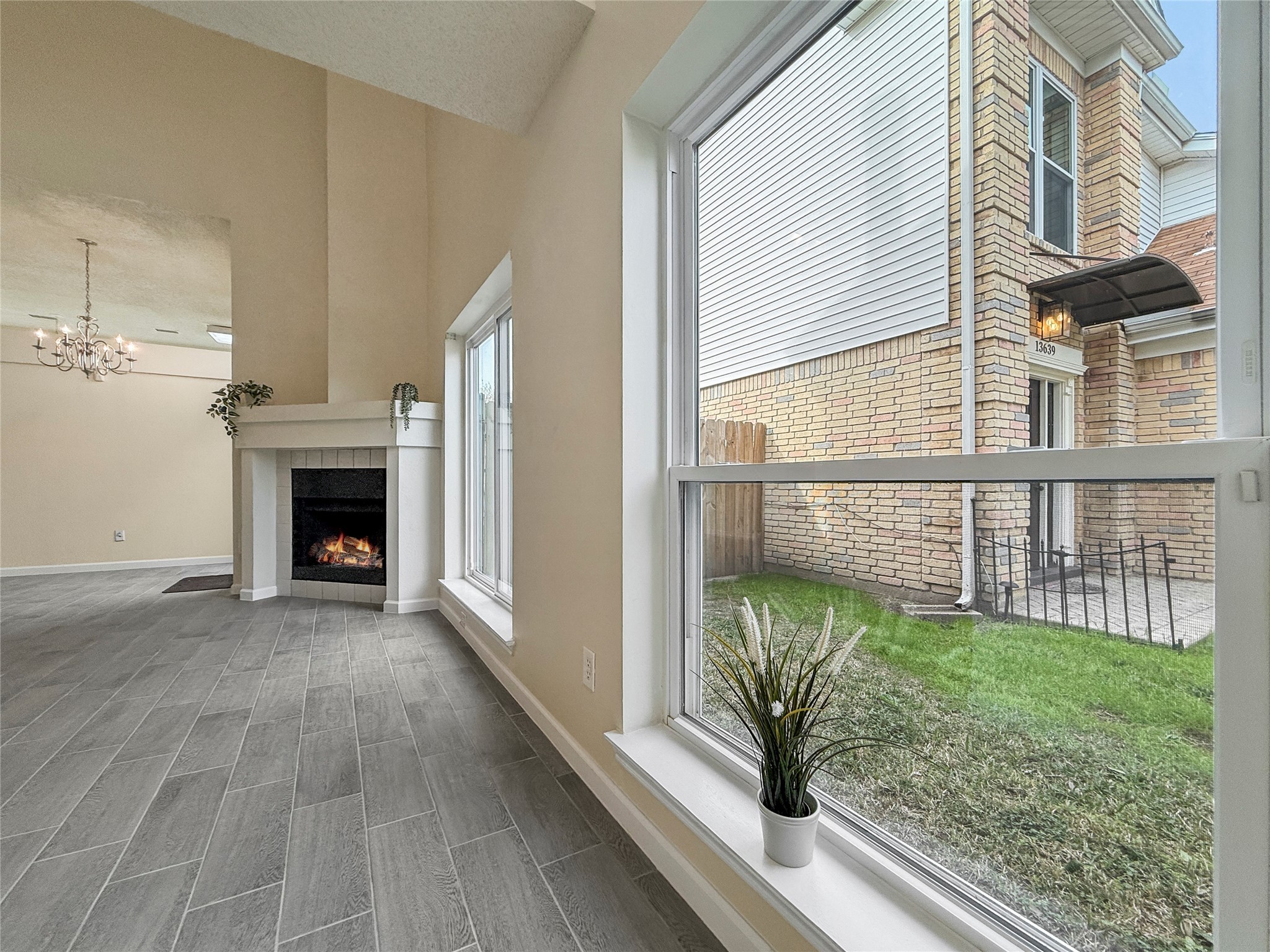 13635 Repa Lane Houston, TX 77014 - Photo 7 of 50 Bright and inviting living area featuring large double-pane windows, a cozy fireplace, elegant chandelier, and modern gray tile flooring. Ideal for relaxation and entertaining.