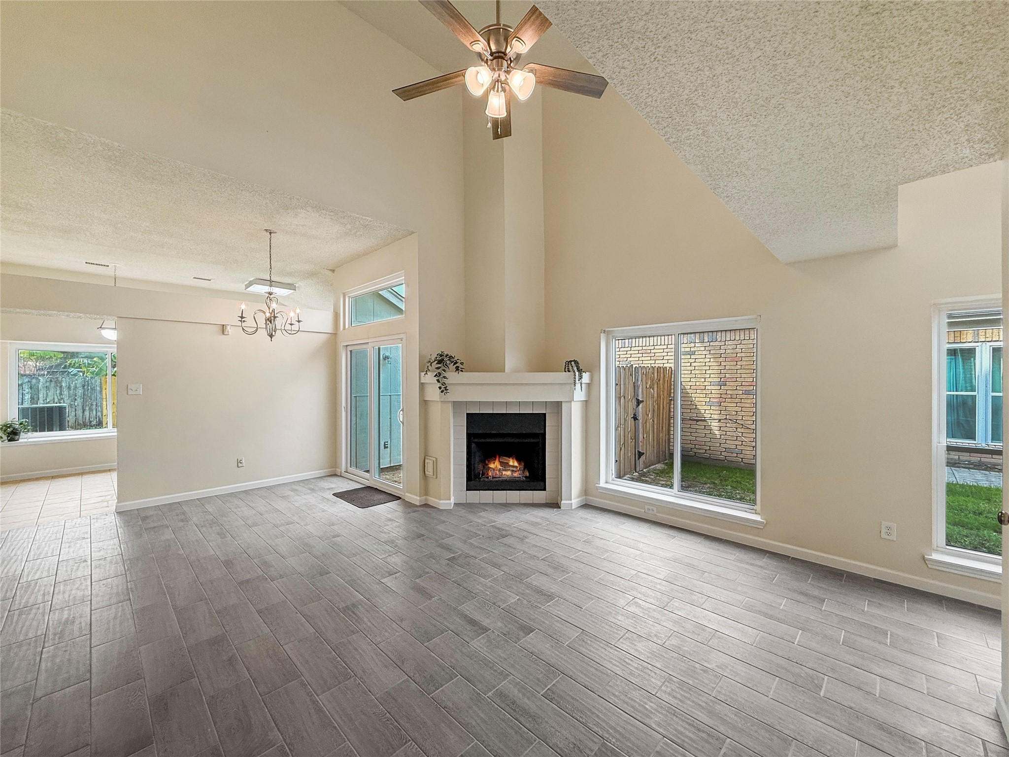 13635 Repa Lane Houston, TX 77014 - Photo 10 of 50 This spacious living area features high ceilings and a cozy fireplace, complemented by large windows for ample natural light. The open layout extends to a dining area with a modern chandelier and access to the backyard. The room is finished with stylish, light-colored flooring, creating a warm and inviting atmosphere.