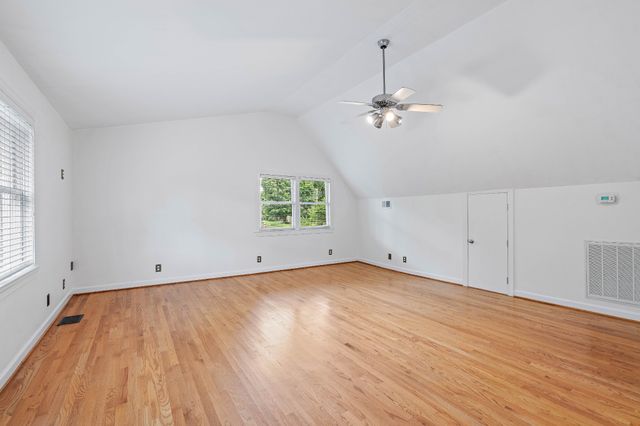 an empty room with wooden floor ceiling fan and windows