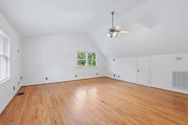 an empty room with wooden floor ceiling fan and windows