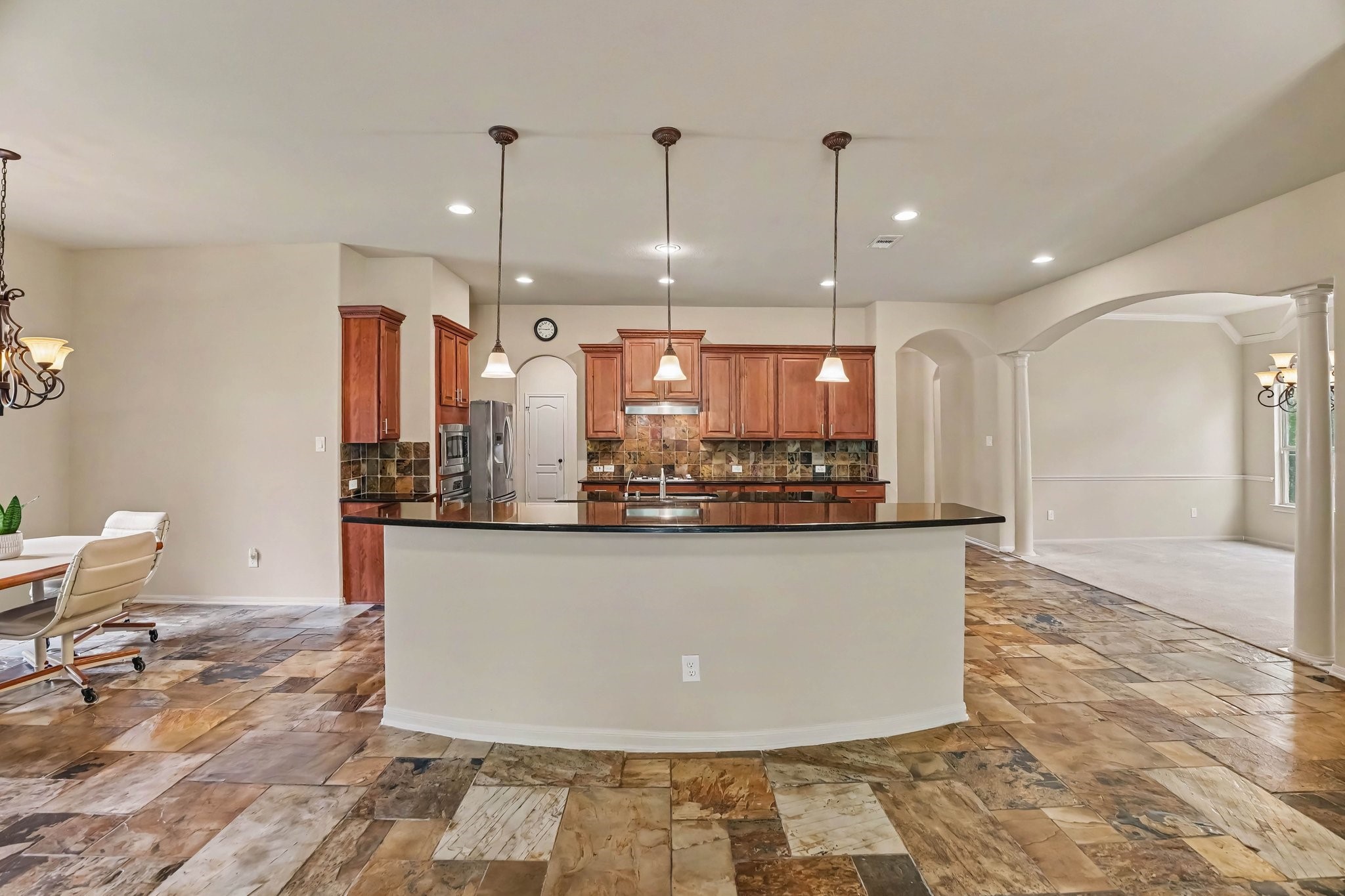 62 Sandwell Place Spring, TX 77389 - Photo 2 of 50 Spacious kitchen with elegant pendant lighting, granite countertops, and rich wood cabinetry, seamlessly connecting to a dining area and open living space.