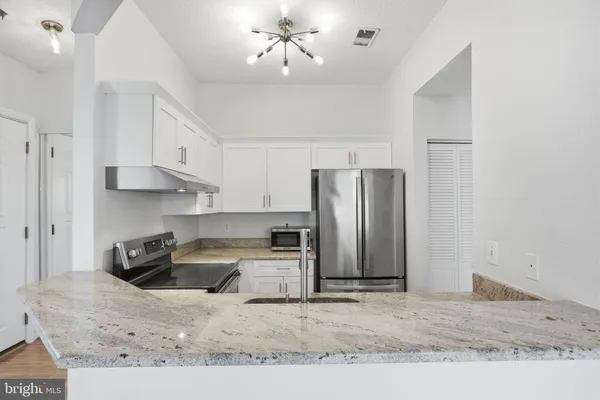 a kitchen with stainless steel appliances granite countertop a refrigerator a stove a sink and white cabinets