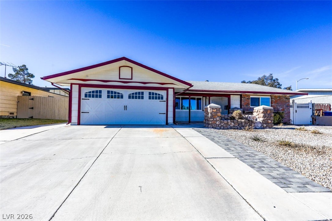 Single story home with a gate, concrete driveway, a garage, and brick siding