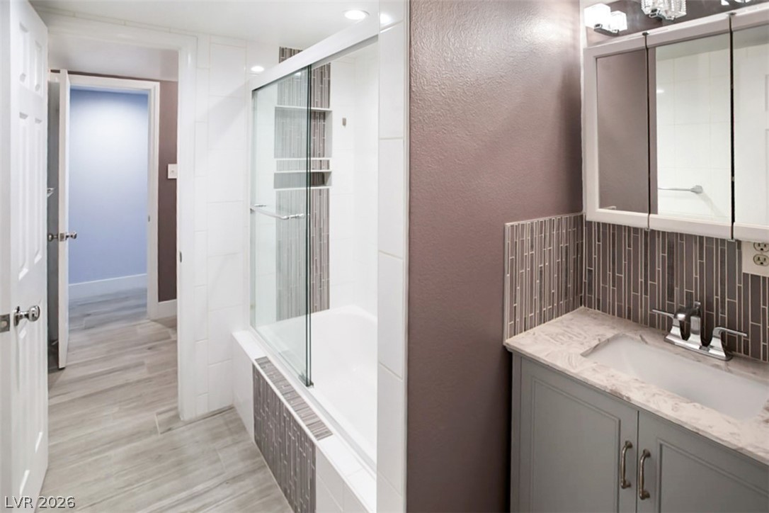 228 Redstone Street Las Vegas, NV 89145 - Photo 15 of 31 Bathroom with vanity, tiled shower / bath, backsplash, a textured wall, and light wood finished floors
