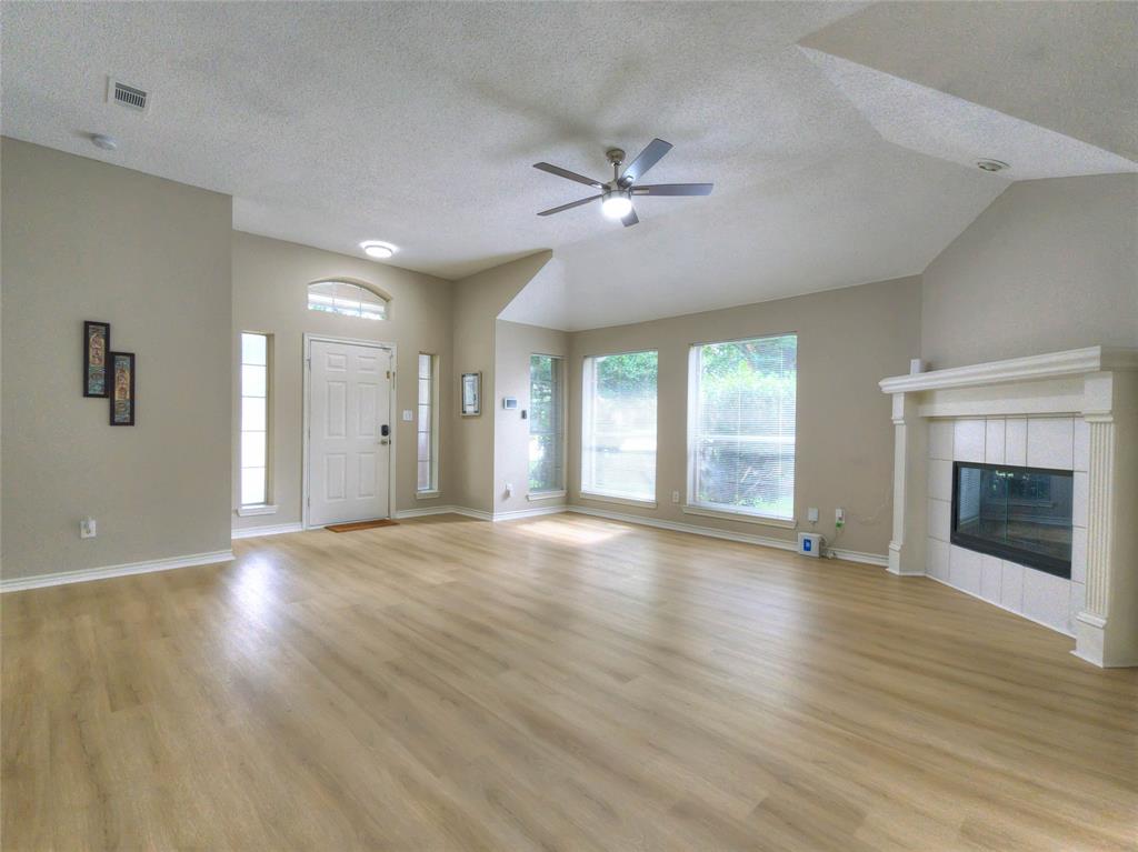 Spacious room featuring light wood-finish flooring, a white fireplace with tile surround, vaulted ceilings, and a ceiling fan