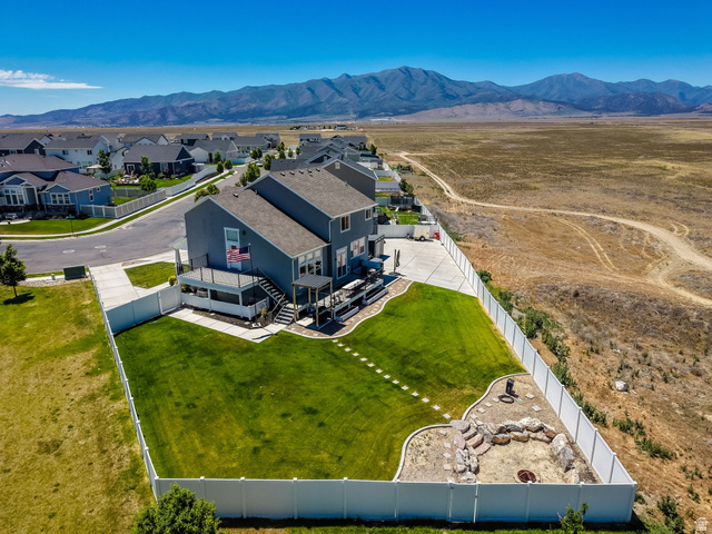 1857 Thunder Gulch Road Eagle Mountain, UT 84005 - Photo 48 of 50 Contemporary gray-sided residence featuring a multi-level deck, expansive fenced backyard with a lawn, and a stone-lined fire pit area