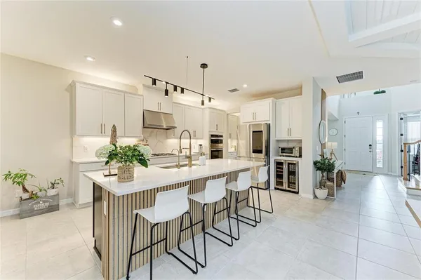 a large white kitchen with stainless steel appliances granite countertop a stove a sink a refrigerator and white cabinets with wooden floor