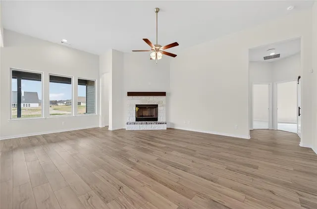 an empty room with wooden floor chandelier fan and windows
