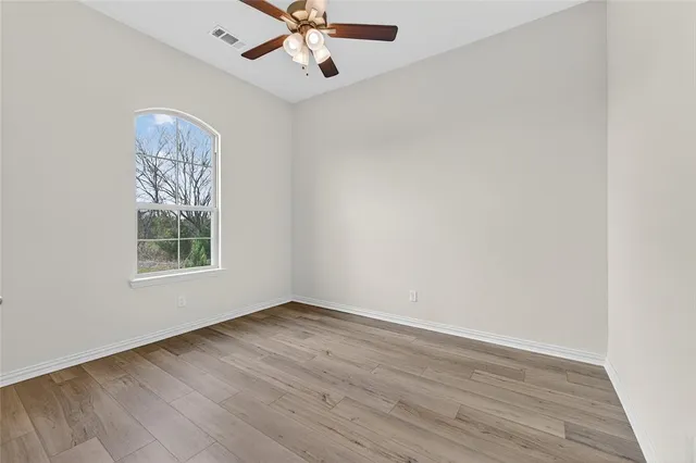 an empty room with wooden floor chandelier fan and windows