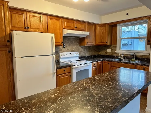 a kitchen with granite countertop a refrigerator a stove a sink a counter space and cabinets